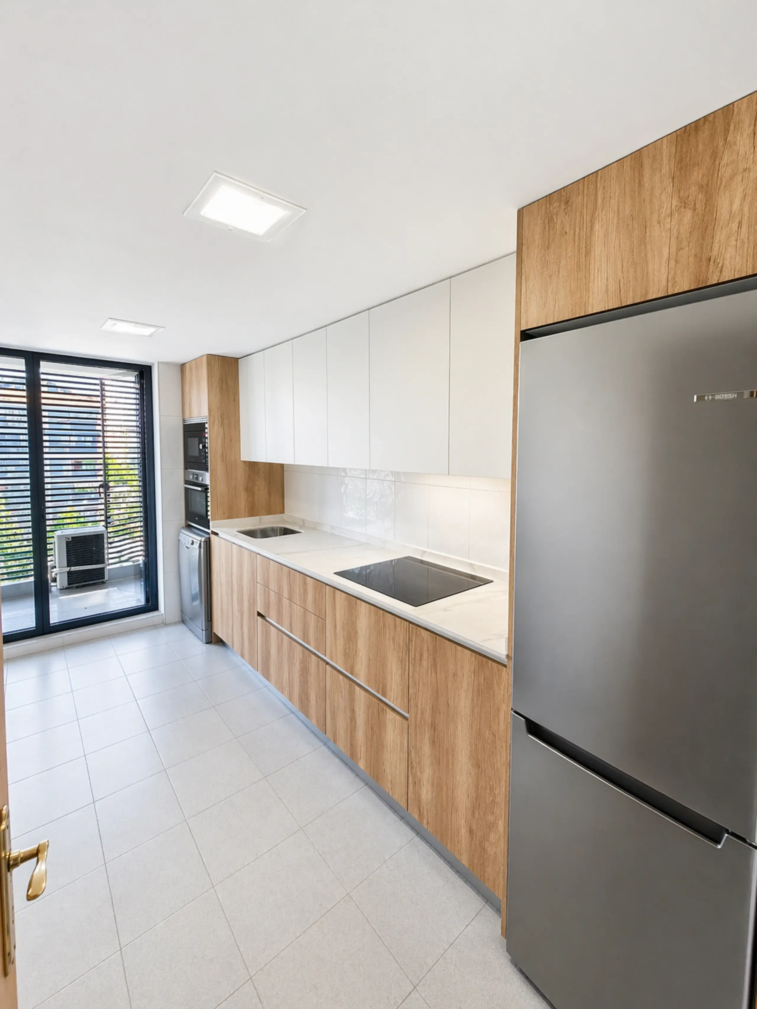 Cocina en línea de madera y blanco con frigorífico de acero y ventana al fondo