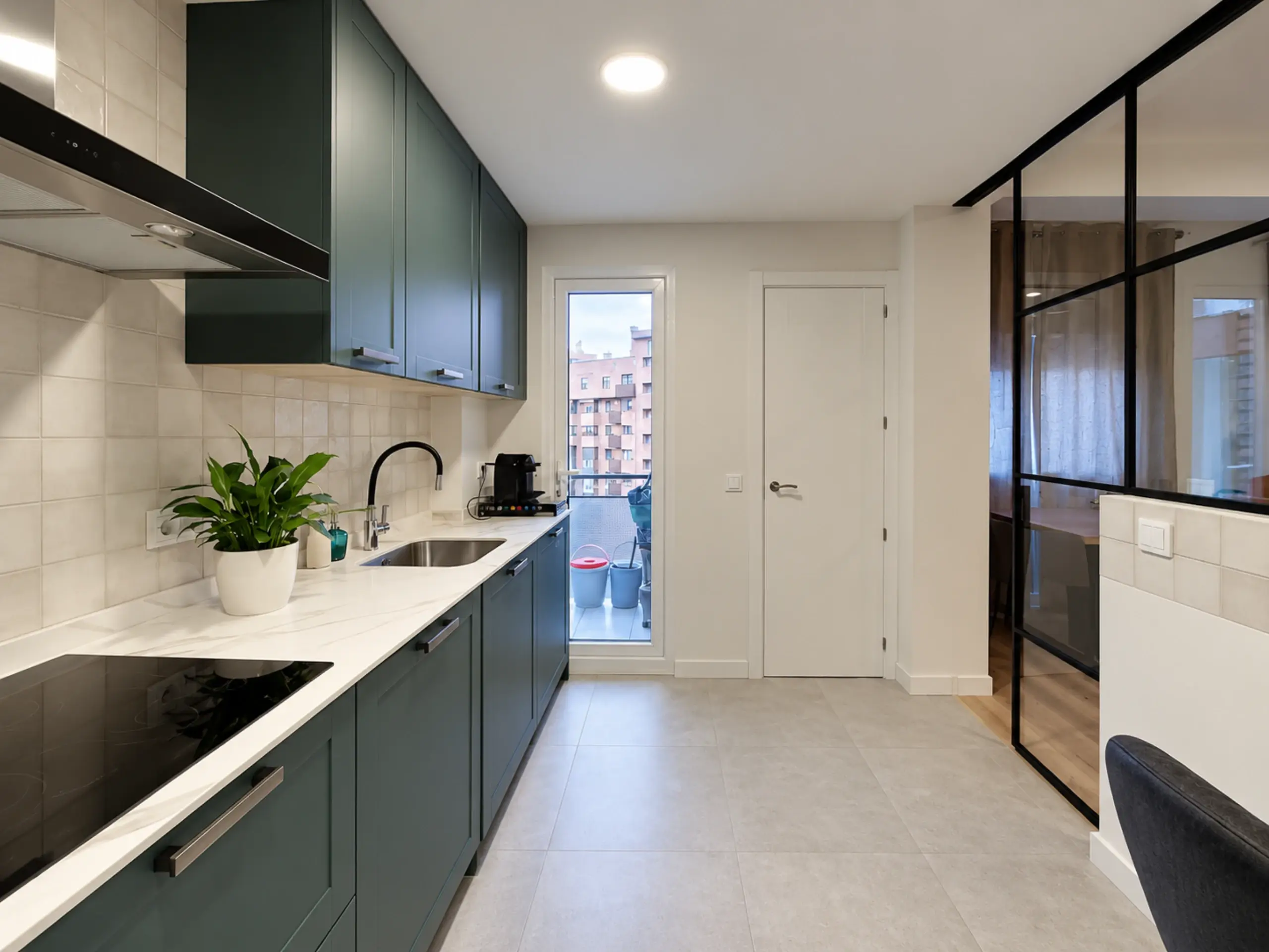 Cocina en línea verde con encimera blanca y puerta de balcón al fondo