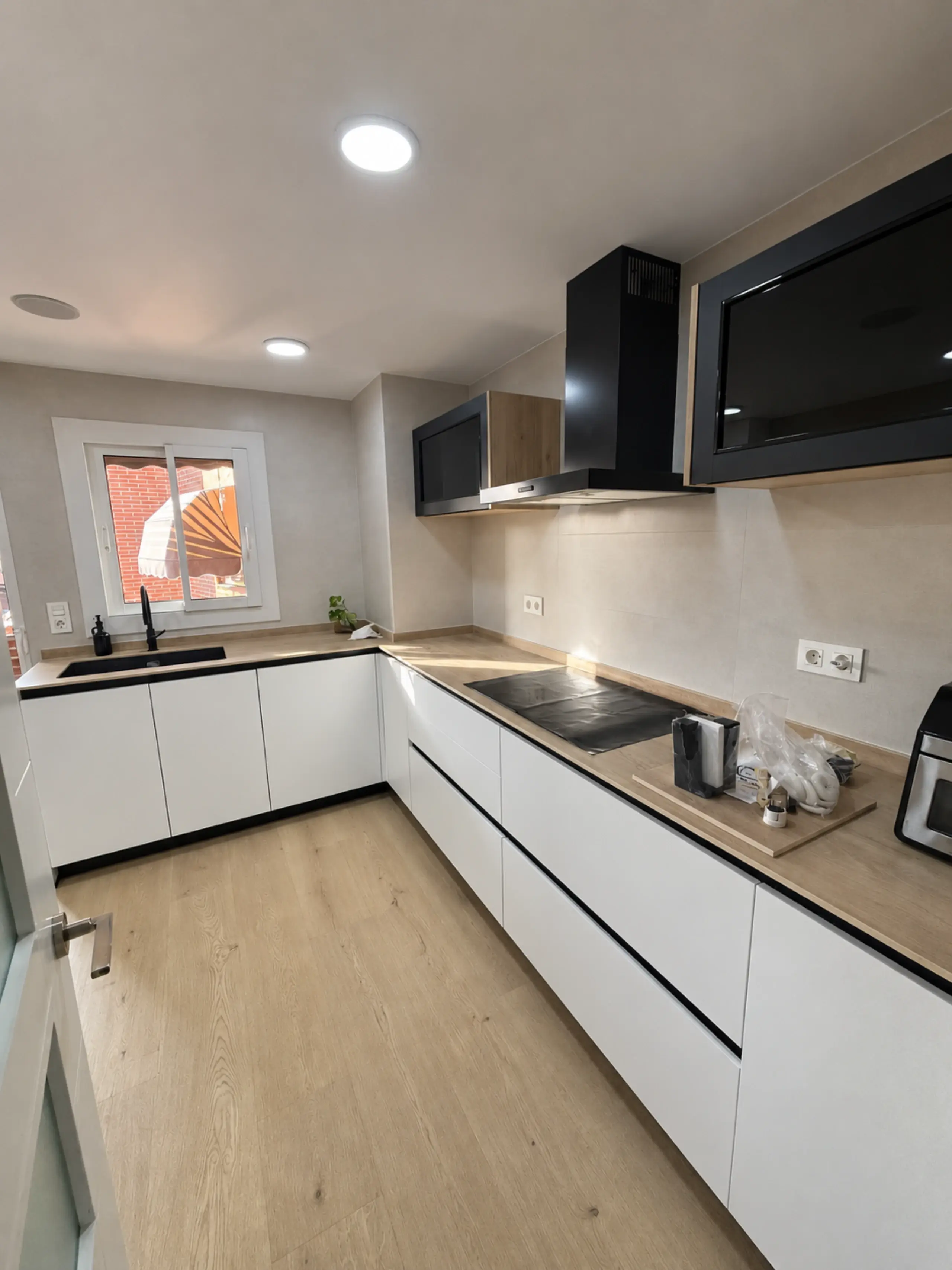 Cocina en L blanca con encimera de madera y muebles altos negros