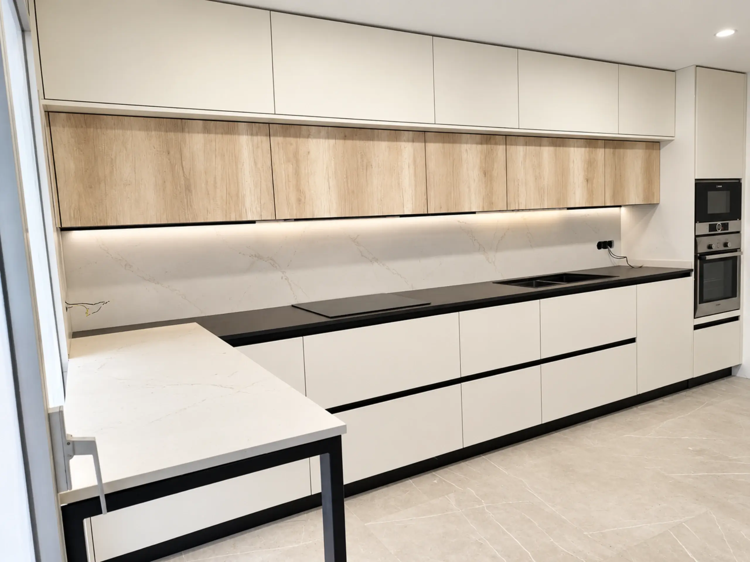 Cocina con península blanca, frente de muebles blancos y franja de madera con luz LED