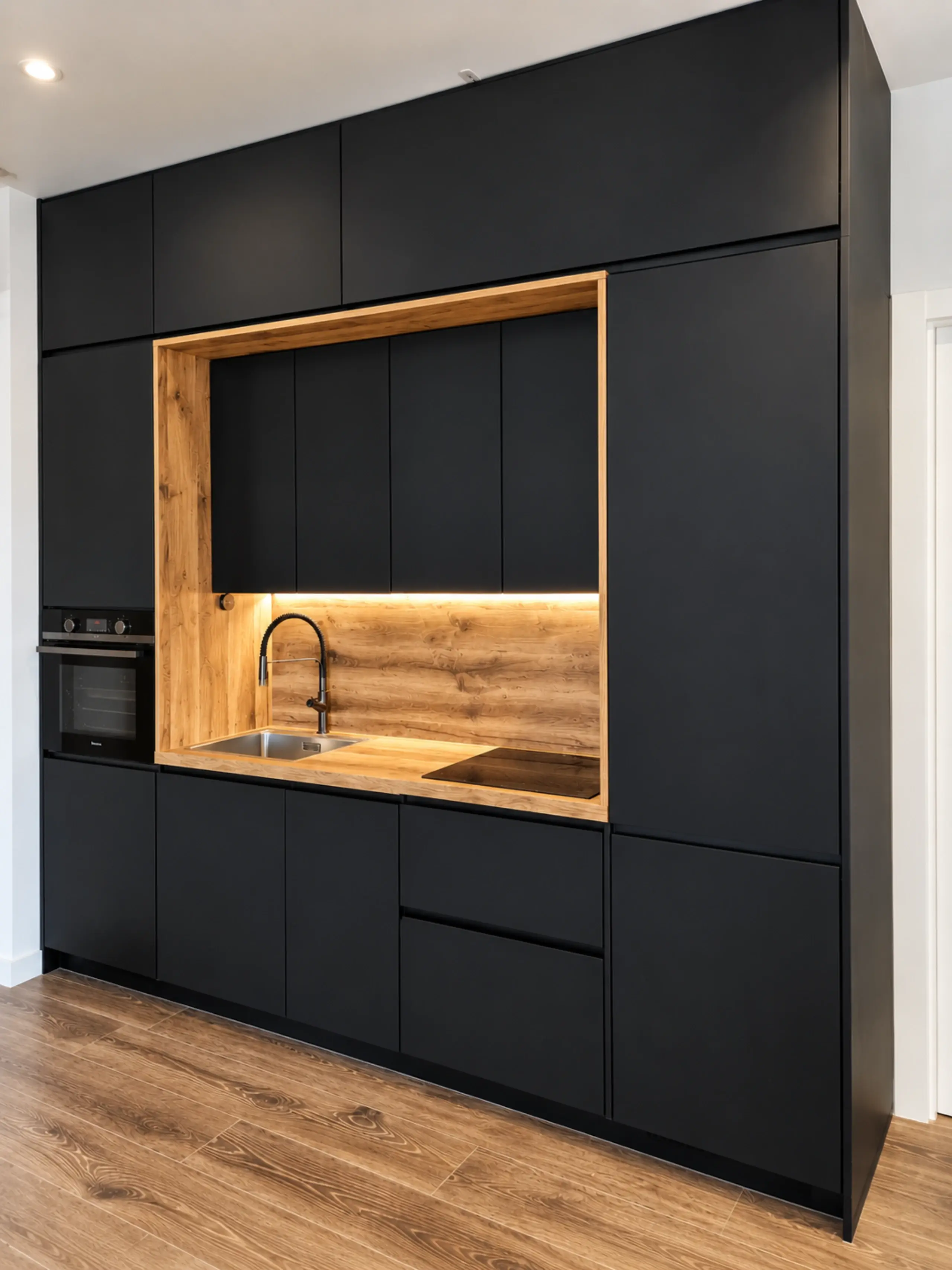 Cocina puente negra vista en ángulo, con el nicho de madera iluminado y cajones sin tirador