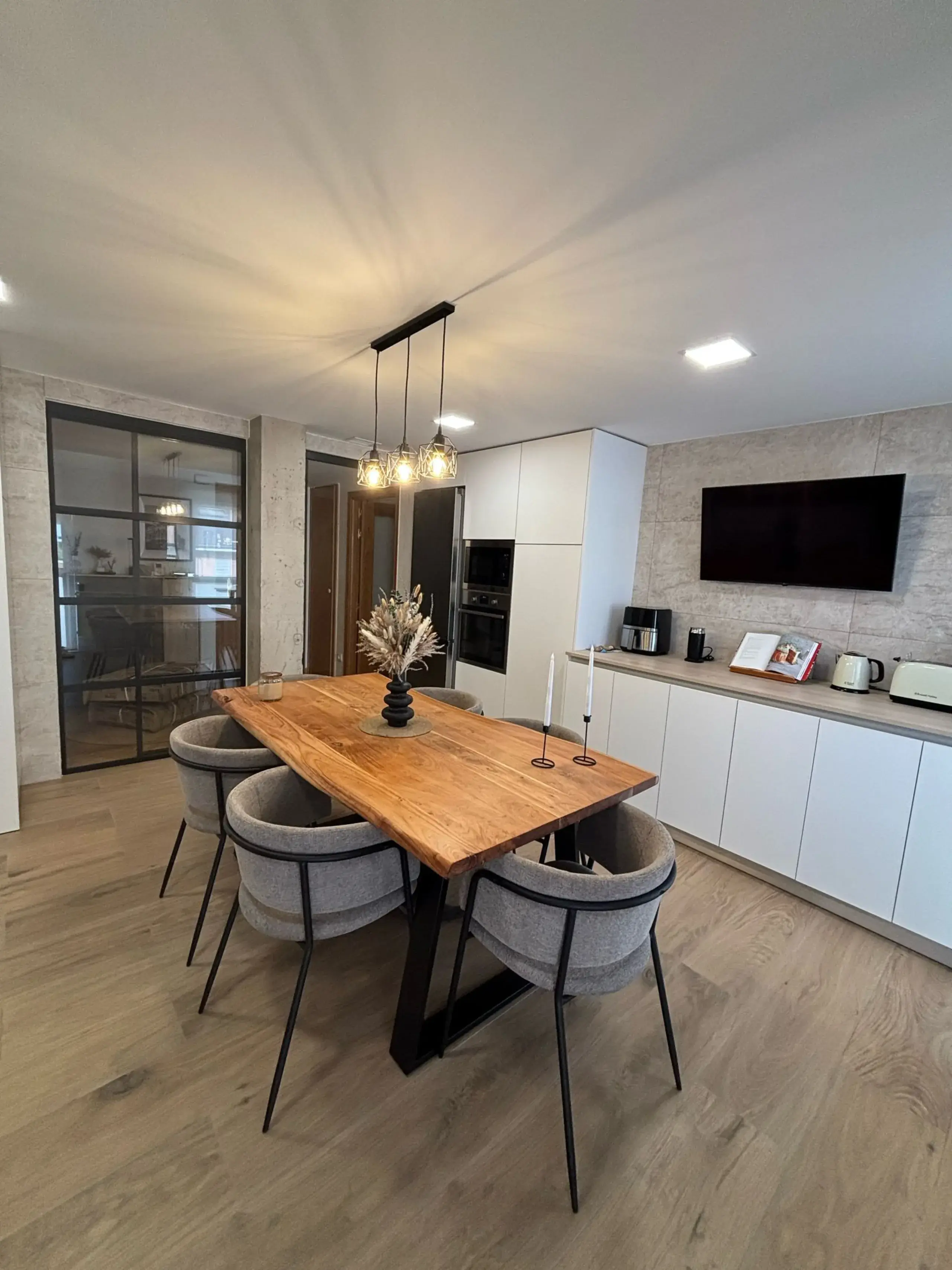 Cocina blanca y madera abierta al comedor, con mesa de madera, sillas grises y lámpara colgante