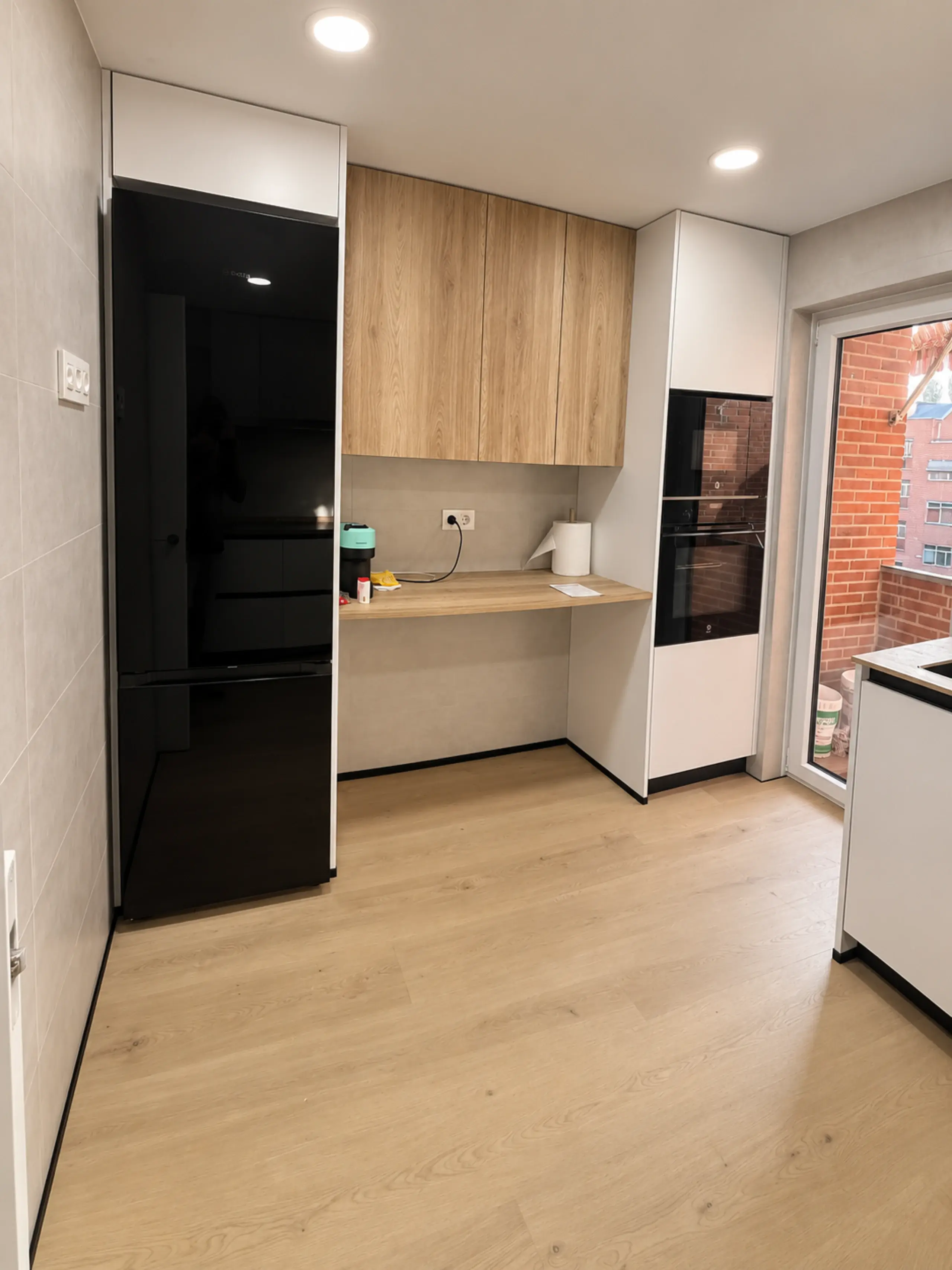 Frigorífico negro, muebles altos de madera y zona de escritorio en la cocina