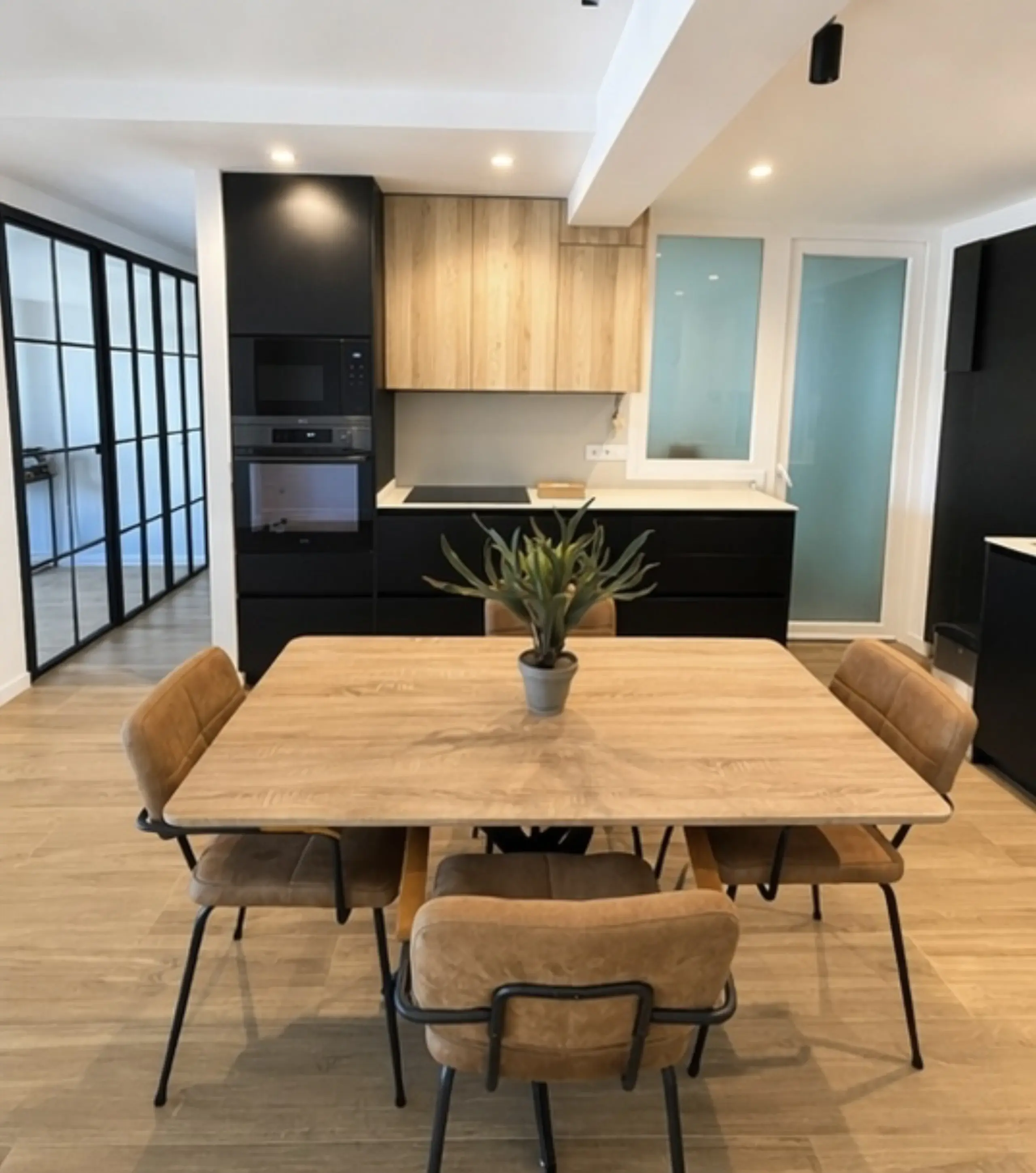 La mesa de comedor con sillas de madera y un cerramiento acristalado de perfil negro al fondo