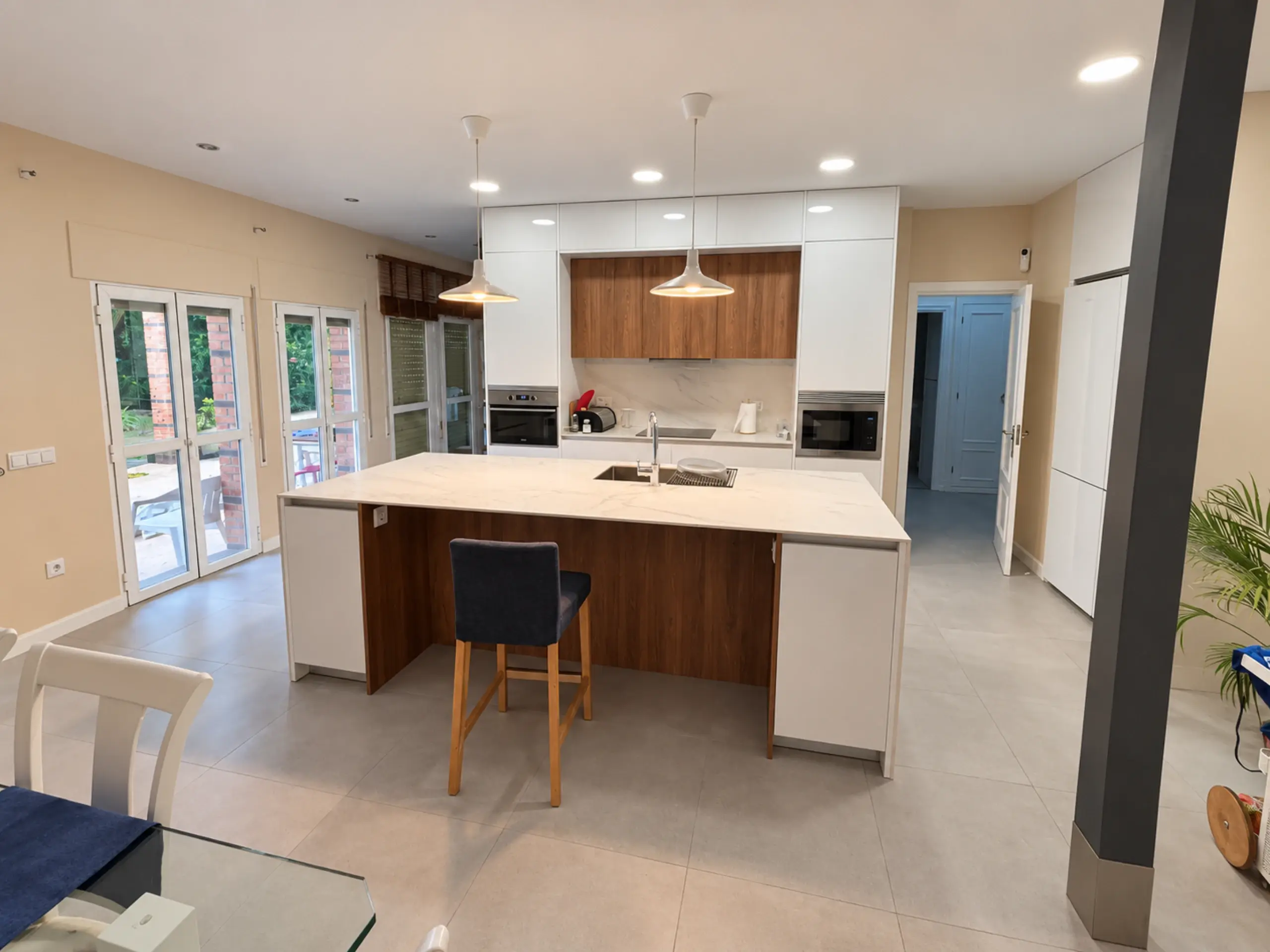 Cocina blanca con isla y muebles altos de madera vista desde el comedor