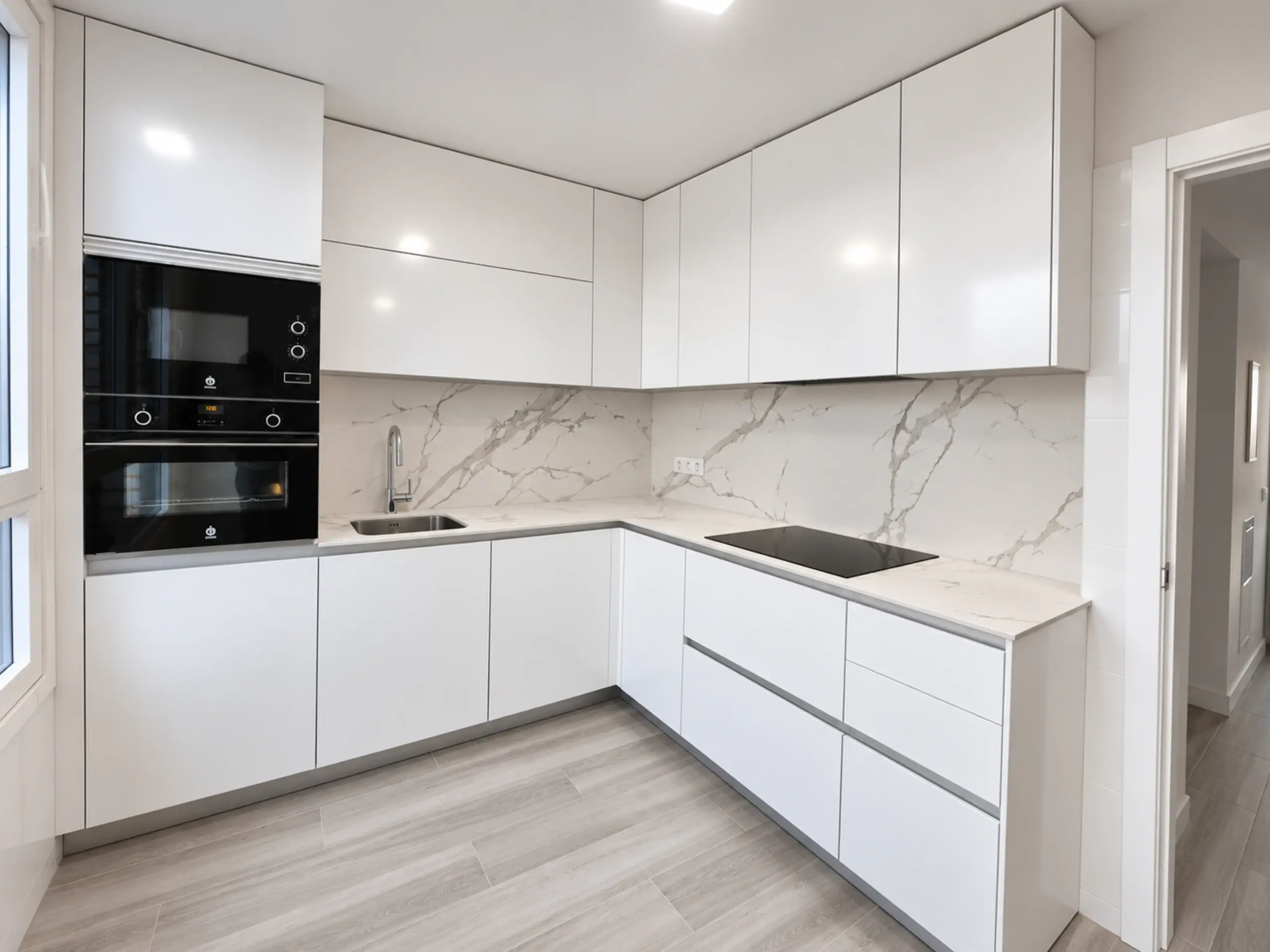 Cocina en L blanca brillo con frontal de efecto mármol y hornos negros en columna