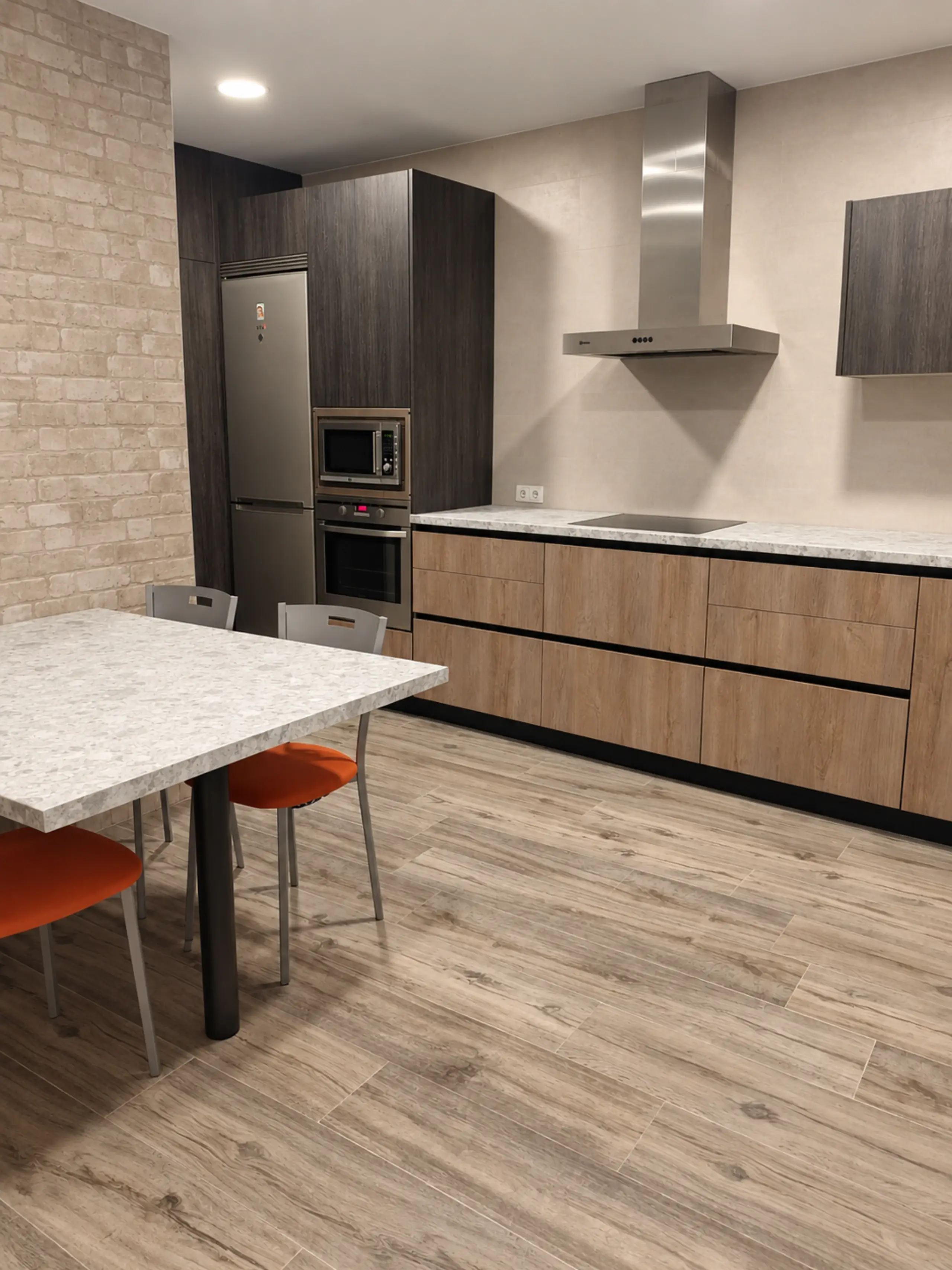 Cocina en L con mesa de comedor, sillas naranjas y una pared de ladrillo visto